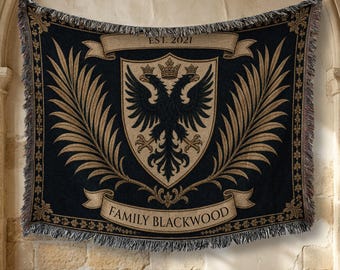 May include: A woven throw blanket featuring a black and tan color scheme with a central shield displaying a double-headed eagle and a crown. The design includes two banners with the text EST. 2021 and FAMILY BLACKWOOD, framed by large palm fronds.