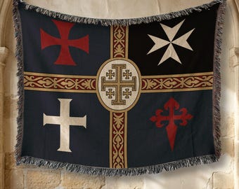 May include: A woven throw blanket featuring a dark background divided into four quadrants, each displaying a different cross symbol in red, white, and black. A central circular emblem contains a gold Jerusalem cross, with fringed edges.