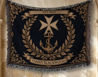 May include: A black woven throw blanket featuring a tan Maltese cross above an anchor, surrounded by a laurel wreath. A banner at the top reads EST. 2021 and a banner at the bottom reads FAMILY BLACKWOOD. The blanket has decorative fringe edges.