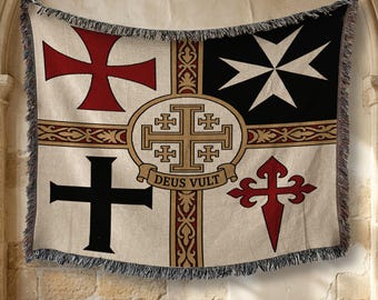 May include: A woven throw blanket featuring a cream background with four distinct crosses in the corners: a red cross pattée, a white Maltese cross, a black Latin cross, and a red cross of Santiago. A central gold Jerusalem cross bears the text DEUS VULT.