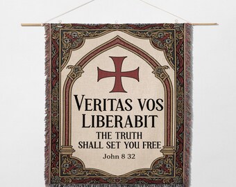 May include: Woven wall hanging with a cream background and a red cross design. The text "Veritas Vos Liberabit" and "The Truth Shall Set You Free" is displayed. The tapestry is framed by ornate borders and a wooden rod.