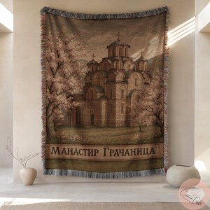 Könnte beinhalten: Gewebte Wandteppich-Wurfdecke mit einer detaillierten Illustration einer Kirche mit mehreren Kuppeln, umgeben von Bäumen mit rosa Blüten. Der Text "Манастир Грачаница" wird unten angezeigt. Die Decke hat einen Fransenrand.