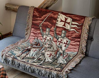 May include: A woven throw blanket featuring a detailed scene of two medieval knights on horseback, each wearing armor and a white tunic with a red cross. One knight holds a sword aloft, while the other carries a flag with a red cross design.