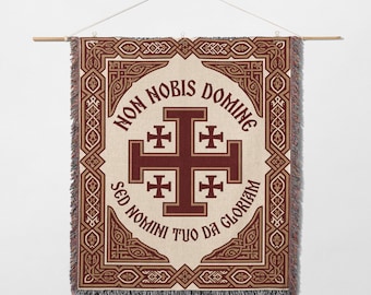 May include: Woven wall hanging featuring a central Jerusalem cross design in burgundy and cream, surrounded by decorative borders and text. The text reads "Non Nobis Domine Sed Nomini Tuo Da Gloriam". The tapestry is suspended from a wooden rod.