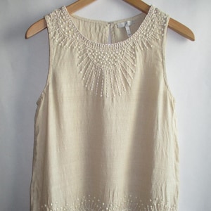 May include: A beige sleeveless linen top with a scalloped hem and pearl bead embellishments around the neckline and hem.