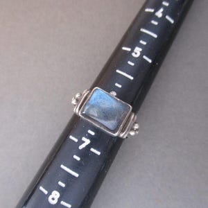 May include: A silver ring featuring a rectangular blue labradorite gemstone set in a bezel setting. The ring band is decorated with small silver beads.