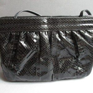 May include: A black snakeskin clutch bag with a fold-over flap and a short shoulder strap.
