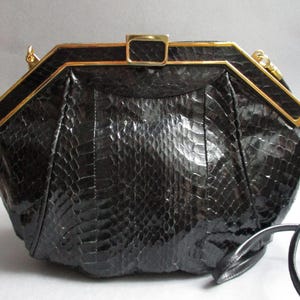 May include: A black snakeskin clutch bag with a gold-toned frame and a long strap.