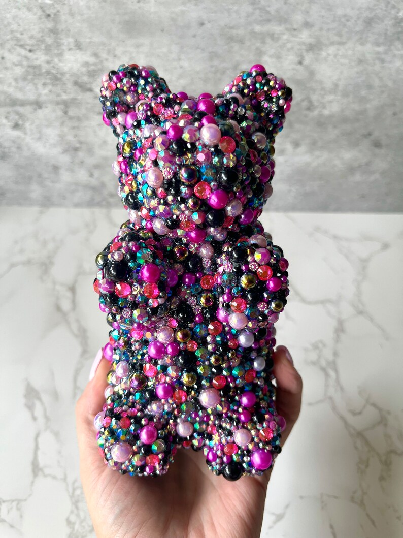 May include: A gummy bear shaped sculpture covered in black, pink, purple, and iridescent beads.