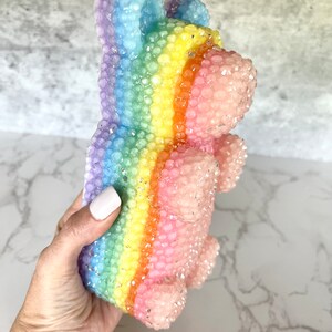 Pu&ograve; includere: Un orso gommoso arcobaleno con una superficie testurizzata. L'orso &egrave; fatto di un materiale trasparente e traslucido e ha una finitura scintillante.