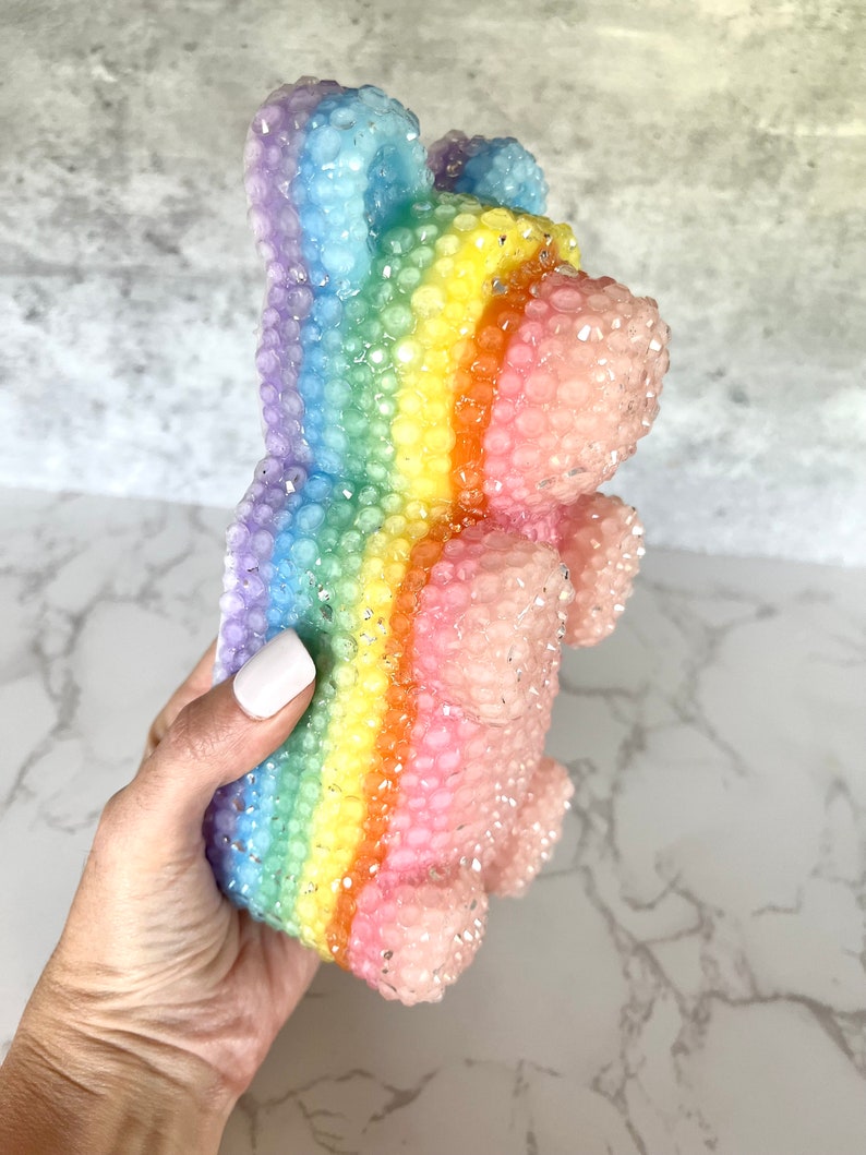 Pu&ograve; includere: Un orso gommoso arcobaleno con una superficie testurizzata. L'orso &egrave; fatto di un materiale trasparente e traslucido e ha una finitura scintillante.