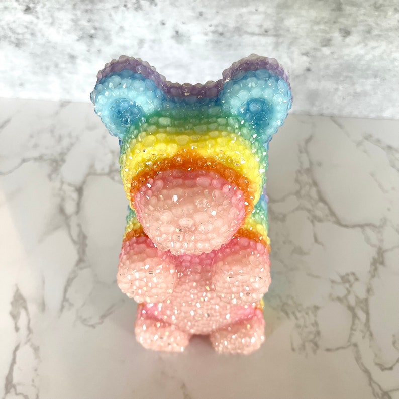 Pu&ograve; includere: Una figurina di orso gommoso arcobaleno con una finitura scintillante. L'orso &egrave; fatto di un materiale traslucido e ha un corpo rosa con una testa arcobaleno.