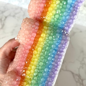 Pu&ograve; includere: Una scultura in resina a forma di pila di blocchi, con una texture a bolle e colori arcobaleno.