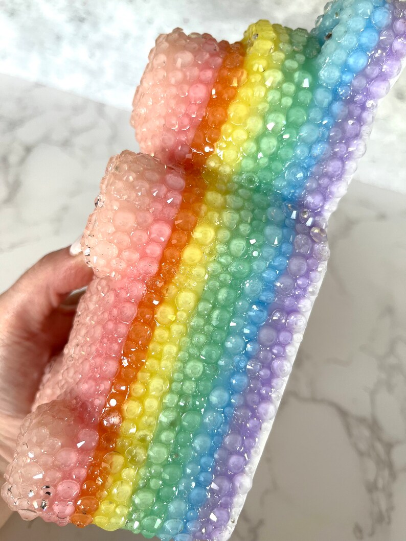 Pu&ograve; includere: Una scultura in resina a forma di pila di blocchi, con una texture a bolle e colori arcobaleno.