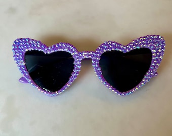 Può includere: Occhiali da sole a forma di cuore di colore viola con strass. Gli occhiali hanno lenti nere.