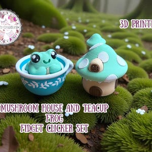 May include: A 3D-printed set featuring a teal mushroom house and a frog in a blue teacup. The teacup and mushroom house are on a bed of green moss. The set is labeled "Mushroom House and Teacup Frog Fidget Clicker Set."