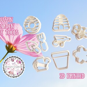May include: A collection of 3D-printed clay tools in various shapes, including a bee, flower, wheelbarrow, and watering can. The tools are white and set against a blue sky background with a pink flower and text that reads "Buzzin Garden Clay Tools".