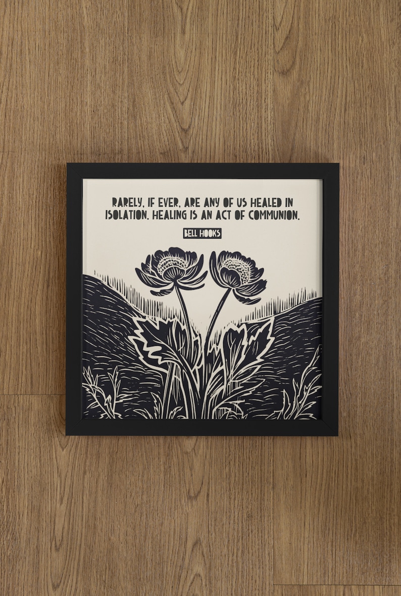 May include: A black framed print with a white background and black text that reads "Rarely, if ever, are any of us healed in isolation. Healing is an act of communion. Bell Hooks". The print features a black and white illustration of two flowers with stems and leaves.