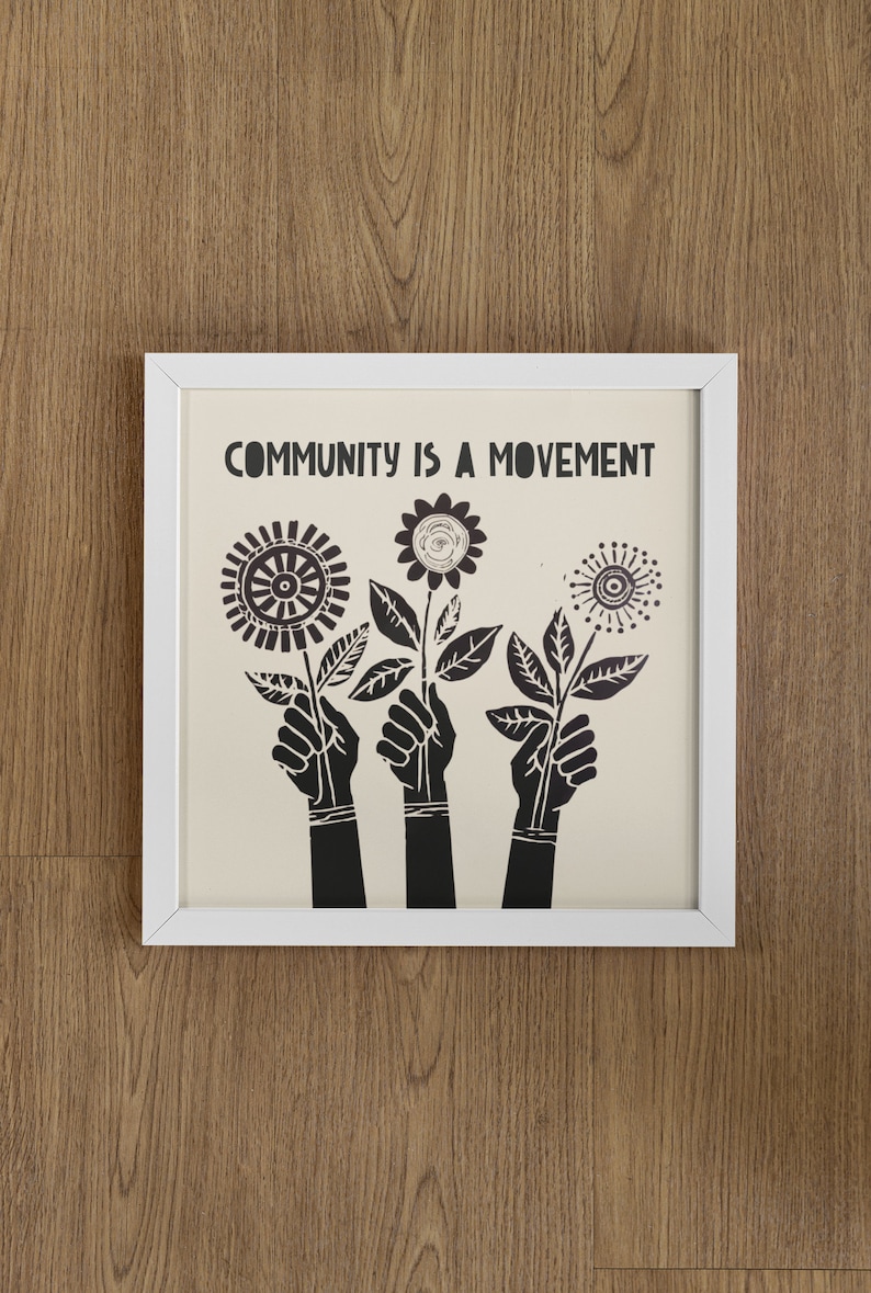 May include: A white framed print with the text "COMMUNITY IS A MOVEMENT" in black lettering. The print features three black silhouettes of hands holding stylized black flowers.