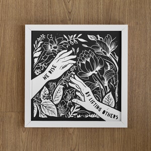 May include: Black and white framed print with a floral design and the text "We rise by lifting others".