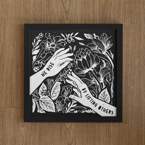 May include: Black and white framed print with a floral design and two hands reaching up. The text "We rise by lifting others" is written on the hands.
