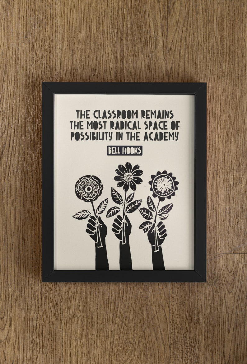 May include: Black and white framed print with the quote "The classroom remains the most radical space of possibility in the academy" by Bell Hooks. The print features three black silhouettes of hands holding stylized flowers.