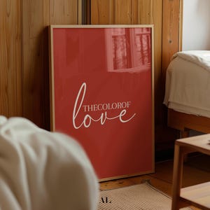 Può includere: Una stampa incorniciata con sfondo rosso e testo bianco che recita "Il colore dell'amore".