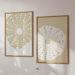 Può includere: Due stampe artistiche incorniciate con un design di riccio di mare. L'opera d'arte presenta una palette di colori beige e bianco, con un motivo dettagliato di piccoli punti e forme. Le cornici in legno aggiungono un tocco naturale all'arredamento.