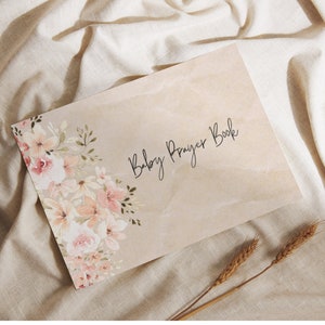 May include: A beige prayer book with the text "Baby Prayer Book" in black script. The cover features a watercolor illustration of pink and white flowers.