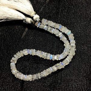 May include: A strand of white moonstone beads with a iridescent sheen. The beads are faceted and have a rectangular shape. The strand is finished with a white tassel.