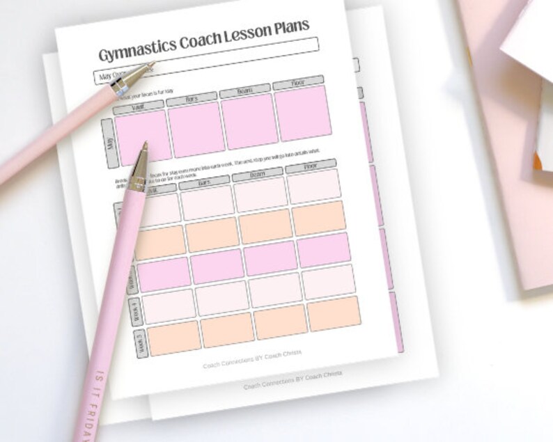 May include: A stack of white Gymnastics Coach Lesson Plans with pink and peach-colored boxes. Two pink pens are on the pages. The text "IS IT FRIDAY" is on one pen. The text "Gymnastics Coach Lesson Plans" is at the top of the page.