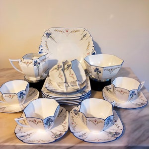 May include: A vintage tea set with white porcelain cups, saucers, and serving pieces. Each item is adorned with blue floral patterns and a blue border. The set includes teacups, saucers, a sugar bowl, a creamer, and a serving platter.
