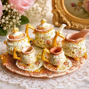 Peut inclure: Un service à thé miniature comprenant une théière, un sucrier, un pot à lait et deux tasses avec soucoupes sur un plateau assorti. Les pièces sont de couleur crème avec des motifs floraux en relief, des anses dorées et des touches roses.