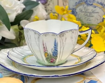Può includere: Un set da tè bianco con bordo blu e motivo floreale. La tazza ha un bordo smerlato e il piattino ha un bordo smerlato. Il motivo floreale presenta fiori blu, rosa e gialli.