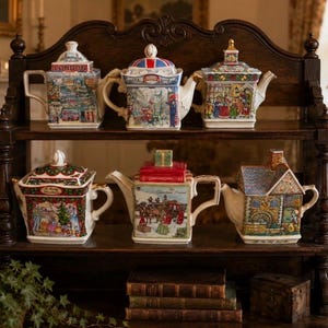 Può includere: Sei teiere decorative in ceramica disposte su uno scaffale in legno a due livelli. La fila superiore presenta disegni a tema londinese, mentre la fila inferiore mostra scene festive, tra cui una teiera a forma di casa e un coperchio a regalo.