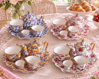 May include: Four porcelain tea sets, each featuring a teapot, teacup, creamer, and small bowl on a scalloped tray. The sets display vibrant floral patterns in blue, pink, yellow, and multi-colored designs with gold-toned rims and handles.