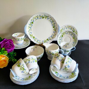 May include: A vintage tea set with a bluebell floral pattern. The set includes a teapot, creamer, sugar bowl, six teacups, and saucers. The teacups and saucers have a delicate blue and white floral design.