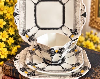 May include: A white porcelain tea set featuring a square plate, a square saucer, and an octagonal teacup. The pieces are decorated with black tree silhouettes, yellow sun accents, and gray landscape borders. The text All Things Shelley is visible.