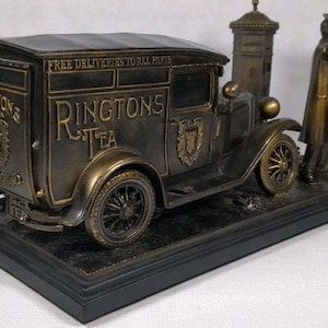Peut inclure: Figurine décorative de couleur bronze représentant un camion de livraison Ringtons Tea vintage, une boîte aux lettres et une figurine en manteau et chapeau. Le camion porte l'inscription "Ringtons Tea" et "Free Deliveries to All Parts". Sur socle noir.