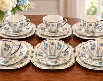 Peut inclure: Un ensemble de six tasses à thé en porcelaine blanche avec soucoupes assorties, ornées d'un motif floral bleu délicat, de bords festonnés noirs et d'un fin quadrillage noir. Les tasses ont une forme facettée et reposent sur des assiettes carrées.