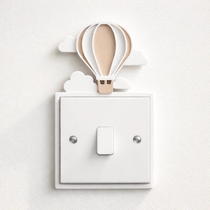 May include: A decorative light switch cover featuring a hot air balloon design. The balloon has a beige center and white accents, with white cloud cutouts. The cover is mounted on a white light switch plate.