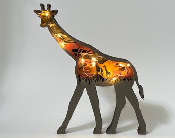 Op de afbeelding: Een houten girafsilhouet met een uitgesneden ontwerp van een Afrikaanse savanne-scène erin. De giraffe is verlicht met warme witte lichtsnoeren, waardoor een gloeiend effect ontstaat.