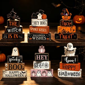 May include: Six sets of stacked wooden blocks for Halloween decor. Each set features themed text like 'The Witch Is In', 'Hey Boo', 'Trick Or Treat', 'Spooky Boo', 'Hey Boo', and 'Happy Halloween', accented with painted ghosts, pumpkins, and bats.