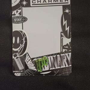 Puede incluir: Una pegatina en blanco y negro con la palabra "CHARMER" impresa en letras blancas. La pegatina tiene un fondo blanco con diseños en blanco y negro alrededor de los bordes. La pegatina está sobre un fondo negro.