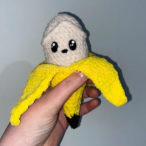 May include: A crocheted banana plush toy with a cute face. The banana is yellow with a black stem and is made of soft yarn.
