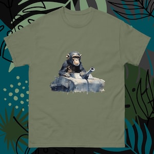 May include: A green t-shirt with a cartoon image of a chimpanzee driving a tank. The chimpanzee is wearing a black shirt and has a serious expression on its face.