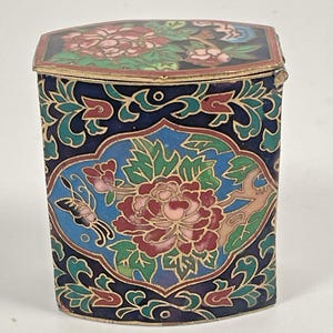May include: A rectangular, lidded box with intricate floral designs. The box features a dark blue background with a central floral motif in red, pink, and green, and a butterfly. The lid also has floral patterns.