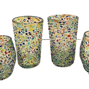 May include: Four colorful glass tumblers with a speckled design. The glasses are clear with a pattern of blue, yellow, red, and green dots. Two are tall and cylindrical, and two are shorter and rounded.