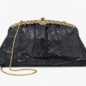 May include: A black clutch with a gold chain strap. The clutch has a textured, snakeskin-like pattern and a gold clasp. The top of the clutch is adorned with a decorative gold trim. The chain is approximately 40 inches long.