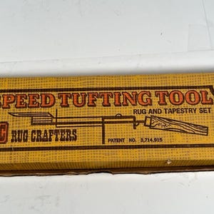 May include: A rectangular box with the words "SPEED TUFTING TOOL" in orange lettering. The box also features the text "RUG AND TAPESTRY SET" and "RC RUG CRAFTERS". The box is a light brown color.